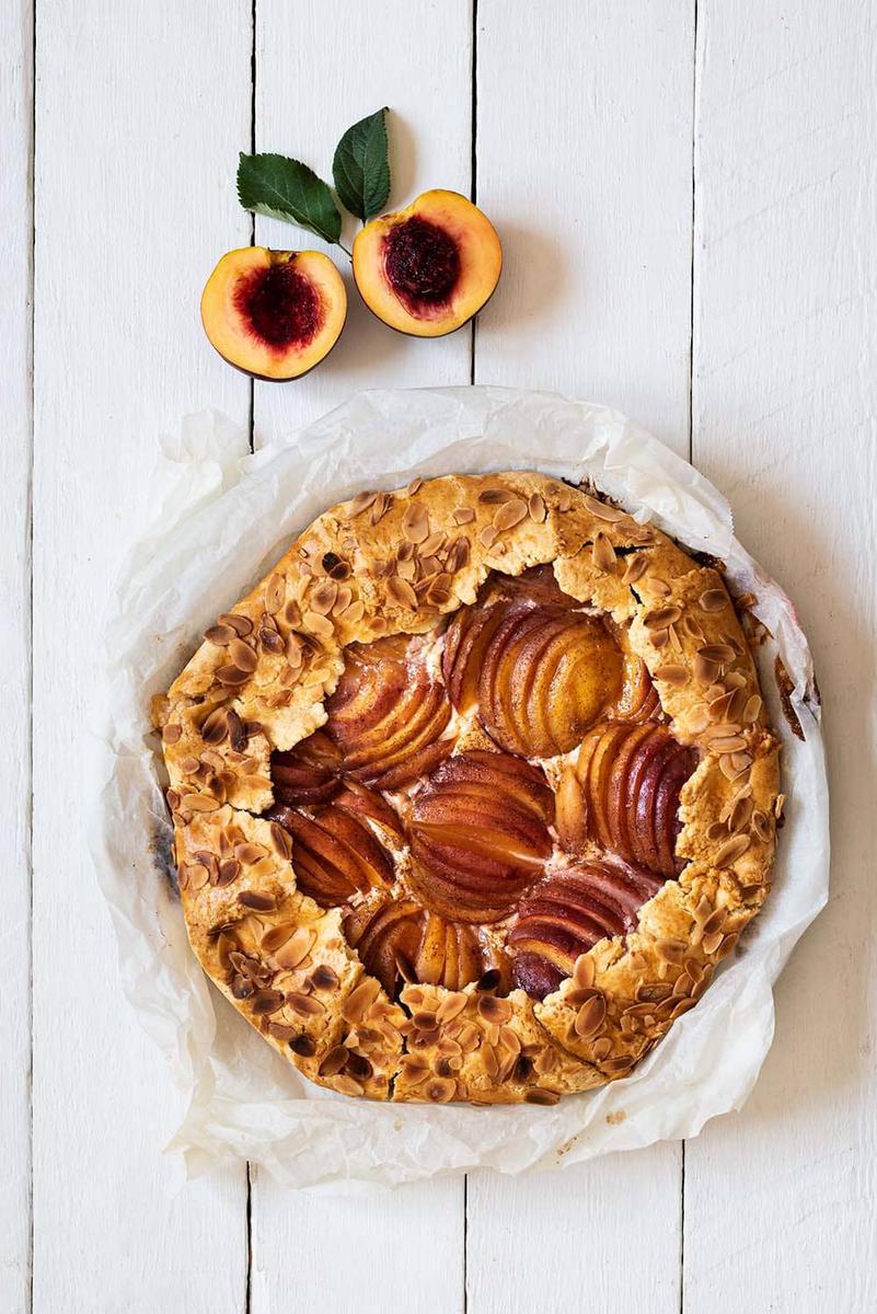 En una mesa de madera blanca está puesto el Galette de nectarina. Alrededor hay una nectarina cortada en la mitad.
