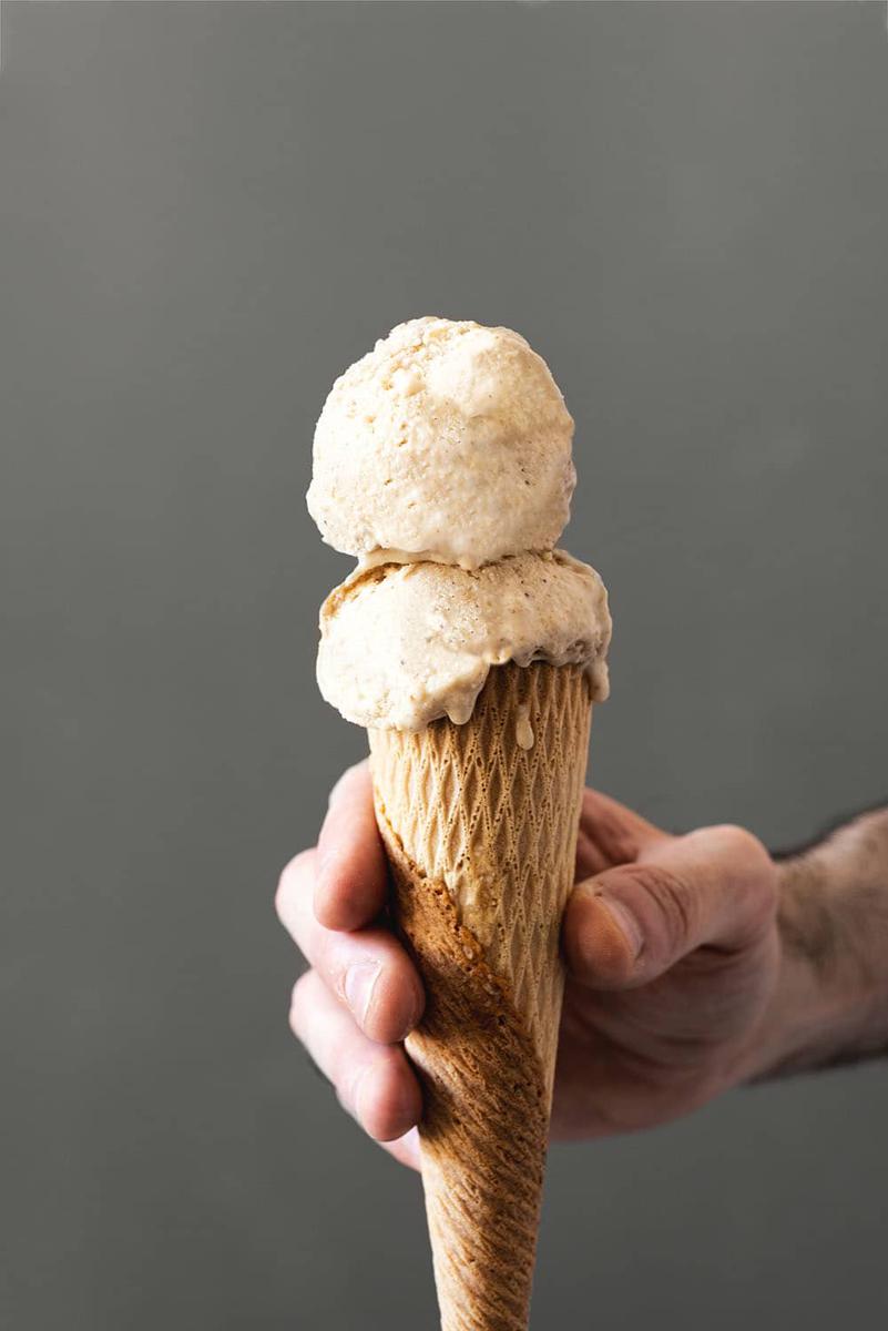 Una mano sujeta un cucurucho. En el cucurucho hay dos bolas de helado de avellana.