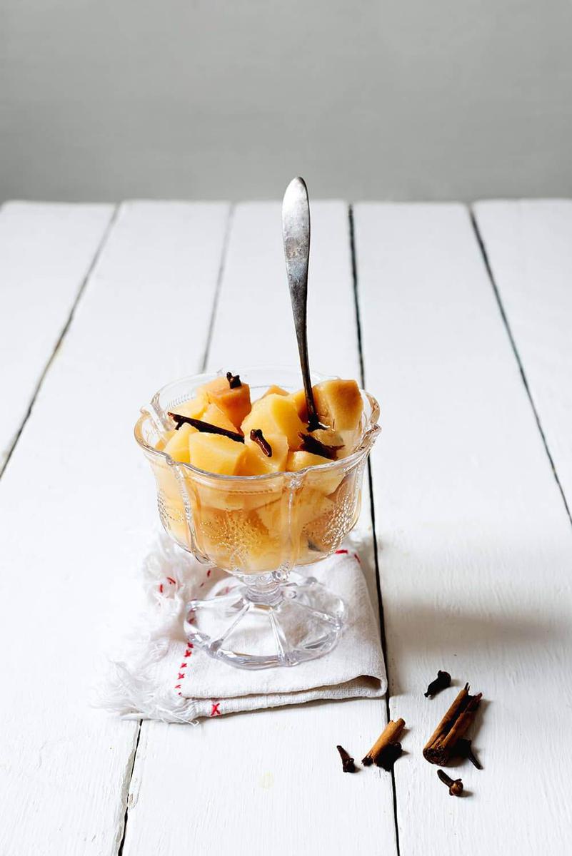 En una mesa blanca está un copa lleno de compota de membrillo. En la copa hay una cuchara.