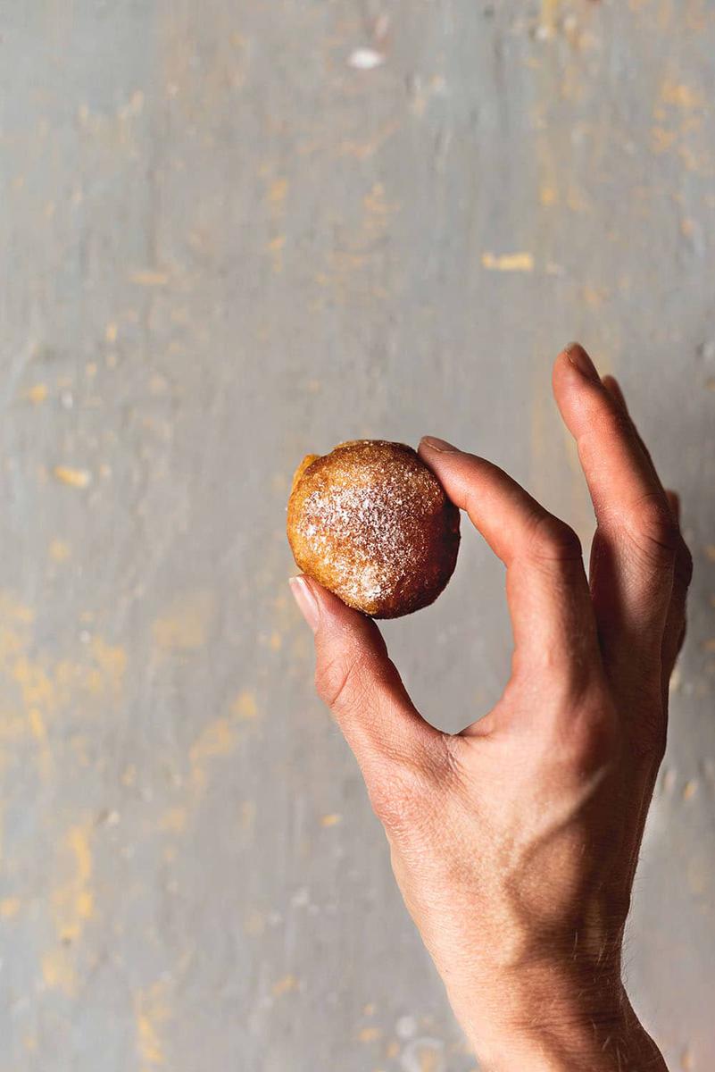 En la mano derecha sujeta un buñuelo de viento casero y esponjoso espolvoreado con azúcar glas.