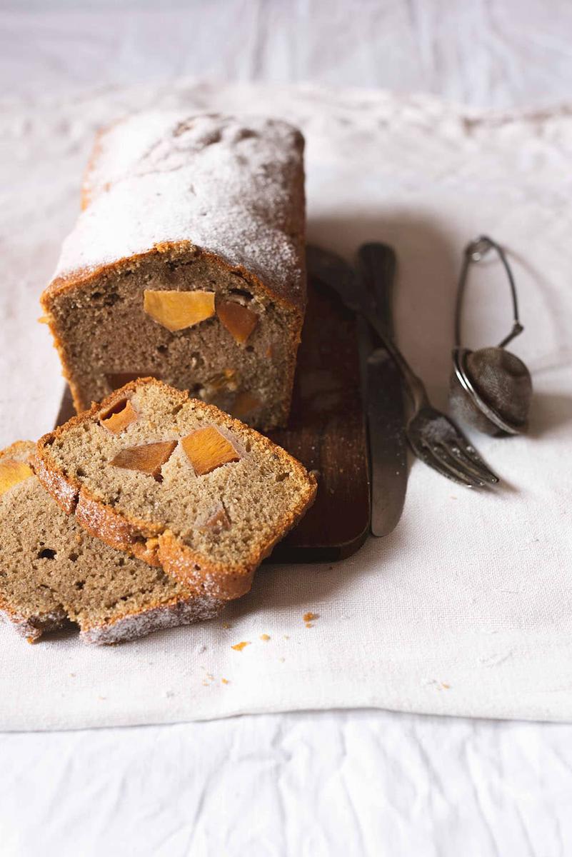 En una mesa cubierta con un mantel blanco, está un trozo de caquis de bizcocho. Al lado hay varios cubiertos.