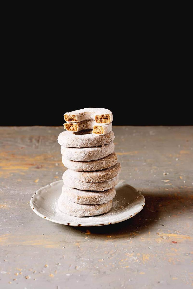En una superficie gris hay un plato blanco. En este plato están varios roscos de vino de la abuela crujientes y caseros para Navidad puestos encima una y otra.