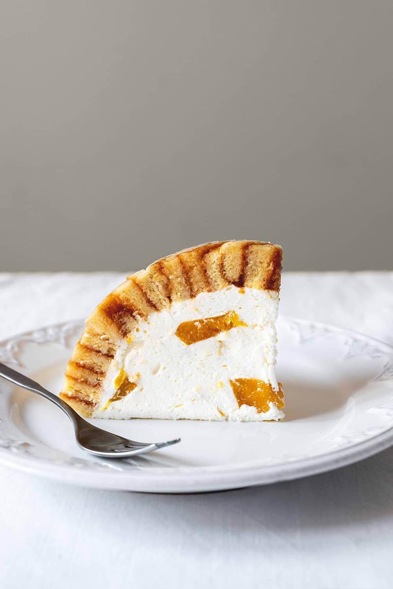 En una superficie blanca está un plato blanco. En el plato está una ración de charlotte royale de melocotón.