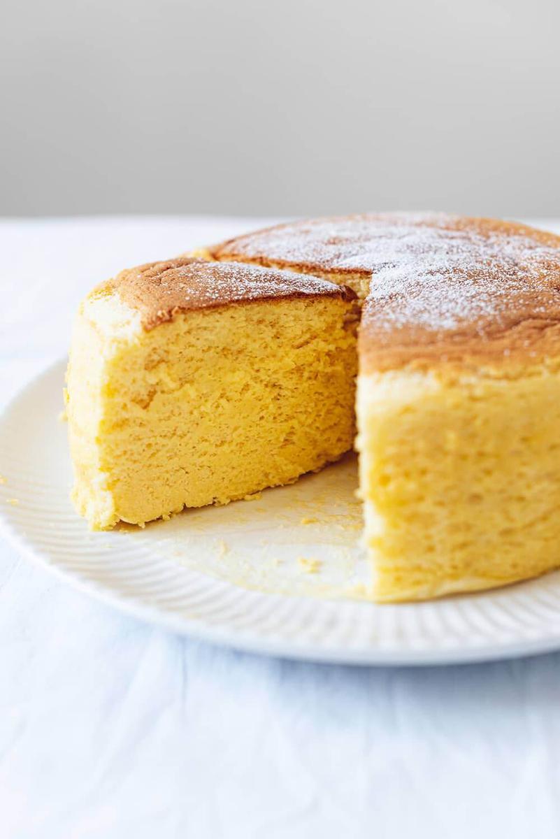 En una mesa cubierta con mantel blanco hay un plato blanco. Encima del plato está el cheesecake japonés esponjoso ya cortado.