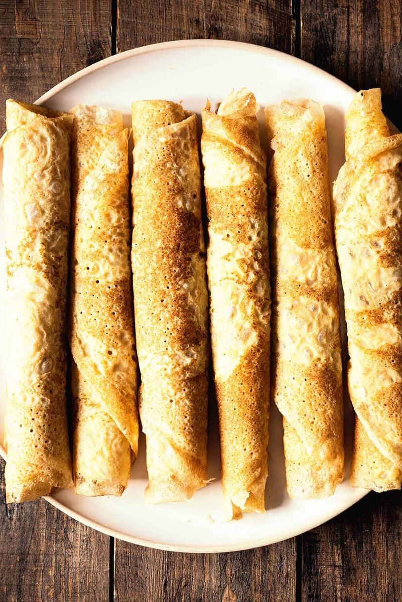 En la mesa de manera hay un plato. En el plato hay varios frixuelos asturianos tradicionales enrollados.