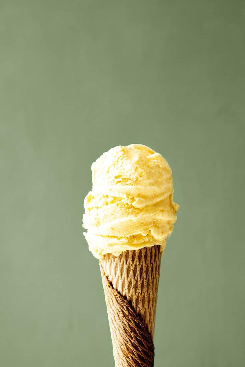 Delante de una pared verde una persona está sujetando un cucurucho lleno de helado de naranja casero. Se ve muy cremoso.
