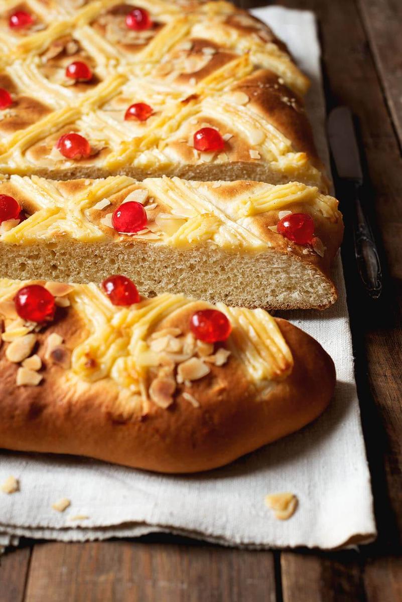 En una mesa de madera está puesto un paño de cocina. Encima está puesta la Coca de San Juan con crema pastelera. Ya está cortada en tiras. Se ve el interior muy esponjoso.