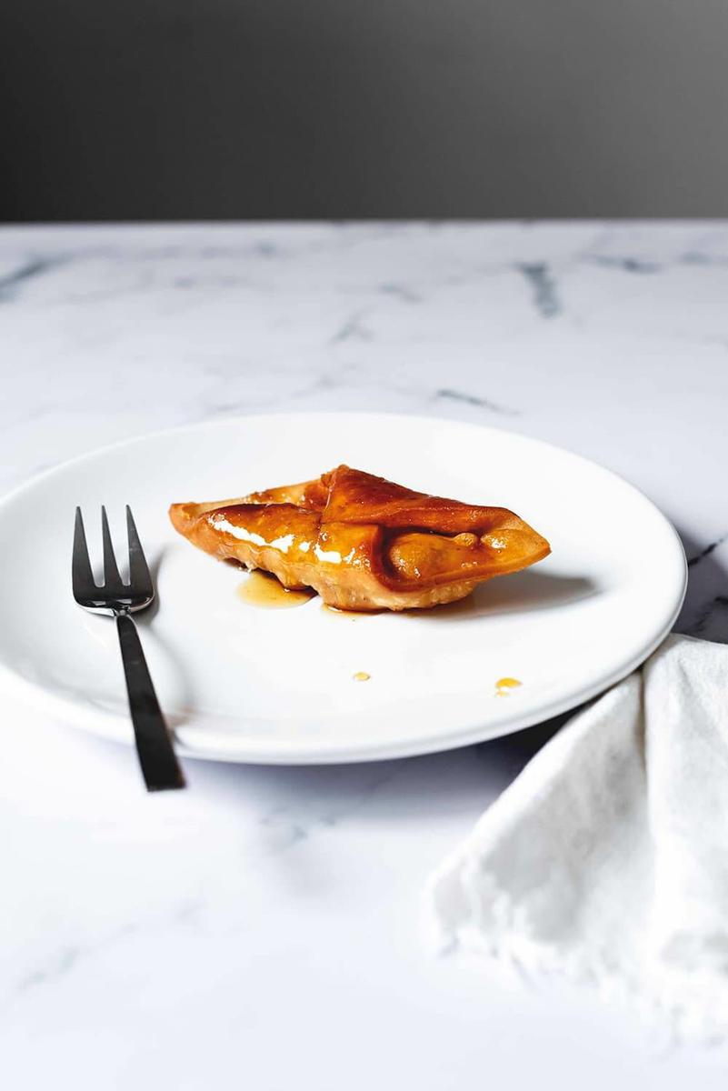 En una mesa de mármol está un plato blanco. En el plato hay pestiños crujientes con miel. Al lado del postre hay un tenedor.