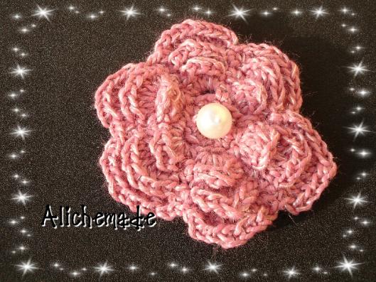 Broche en forma de flor, rosa, con una perla en el centro.