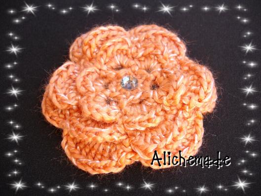 Broche en forma de flor, naranja con brillante en el centro.