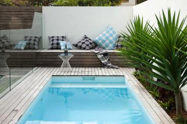 Piscina con barandilla de cristal sin juntas, banco a medida con cojines a modo de tumbona