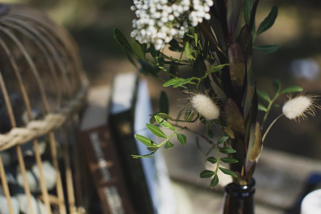 La mesa situada en pleno bosque acoge un banquete en petit comité. La vajilla, las hojas con nombres de árboles escritos a mano y las flores en botellas de cristal aportan delicadeza y calidez a la decoración. Mientras que las hojas secas, los troncos y la mesa de madera natural aportan la esencia propia del otoño. Las frutas de temporada también toman protagonismo en esta celebración tanto en la decoración como en el postre.