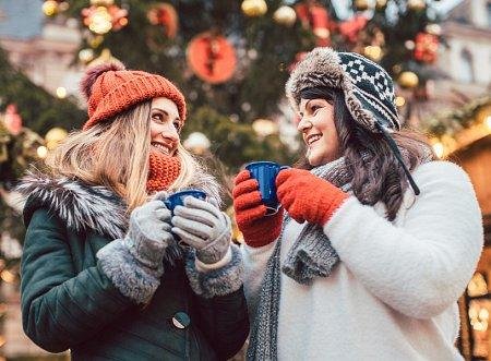 Dos amigas toman bebidas calientes al aire libre en invierno